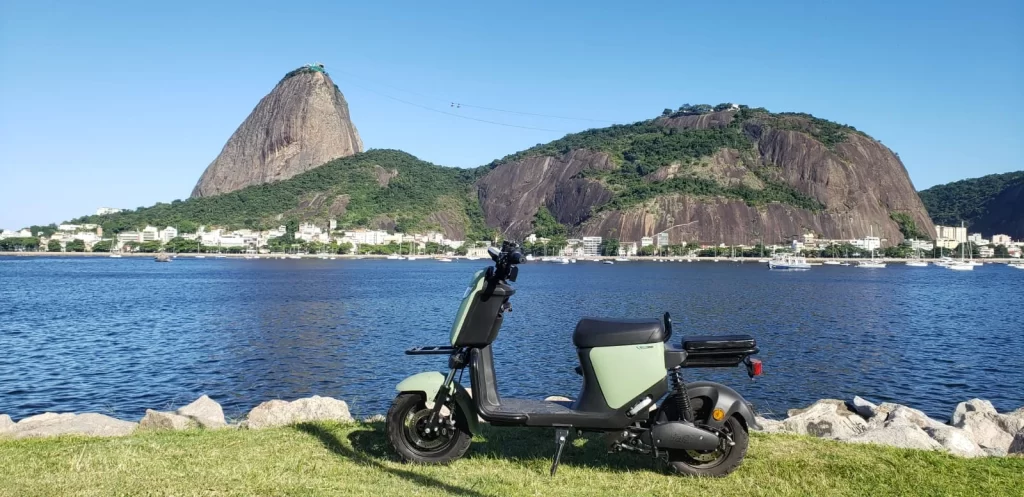 Moto elétrica verde e preta parada na frente de uma praia no Rio de Janeiro em um dia de sol.